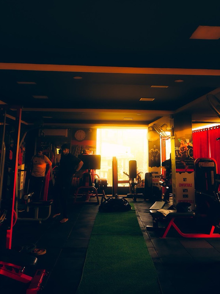 The gym in the half-dark with red-lit racks and daylight at the far window